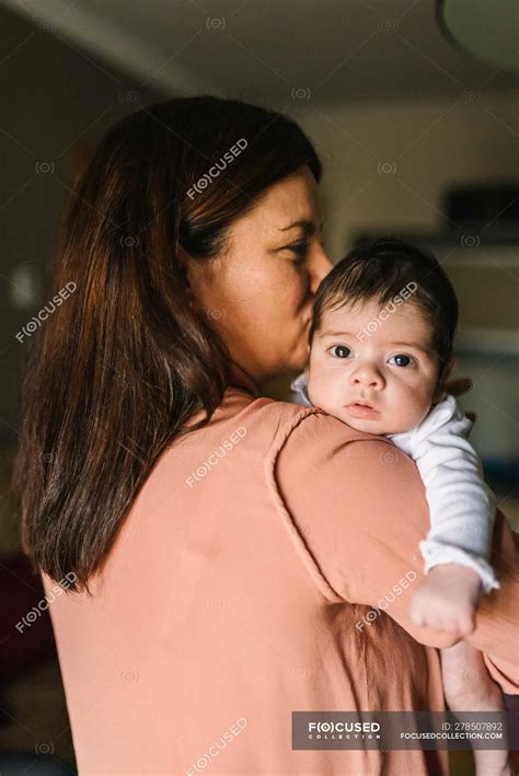 Back view brunette mom hugging cute little baby looking away at home