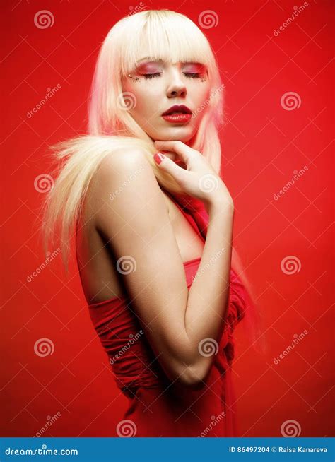 Perfect Blond Model in Red Dress Over Red Background. Stock Photo