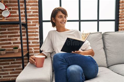Young Beautiful Hispanic Woman Reading Book and Drinking Coffee Sitting