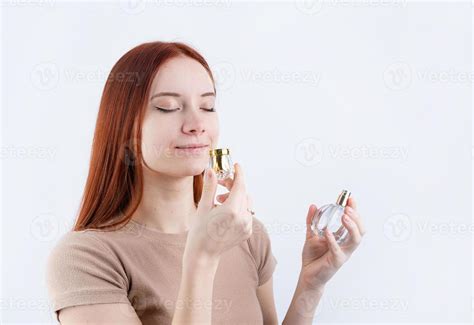 happy young woman smelling perfume holding glass bottle isolated