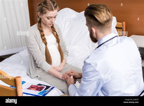 Bearded man doctor reassuring upset pregnant woman sitting on hospital ...