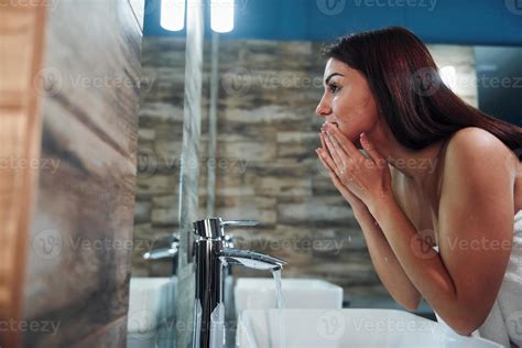 Beautiful young woman standing in bathroom near the mirror and washing