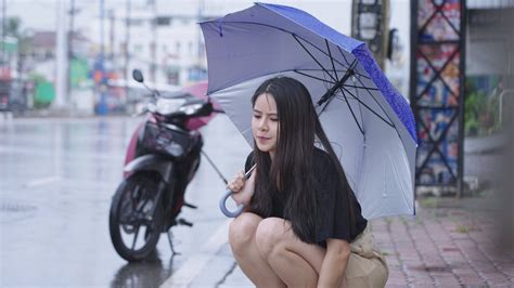pretty asian girl holding umbrella sit down on the street side walk on