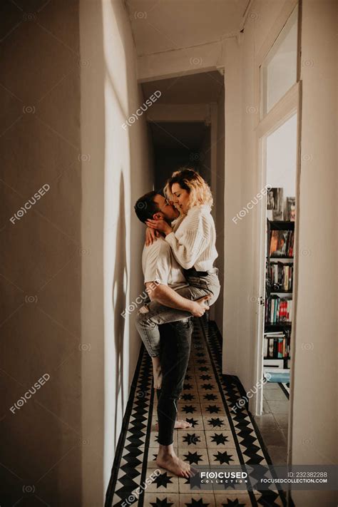 Passionate man and woman embracing and kissing at wall in hall at home