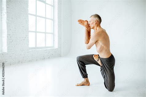 Senior athletic man with naked torso practising yoga poses in the white
