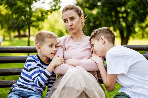 Mother is sitting with her sons on bench in park. She is angry and the