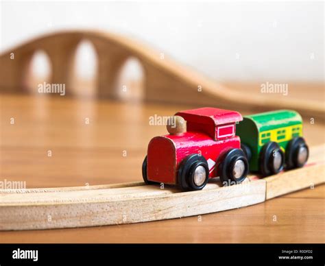 Red and green wooden toy train on railroad with bridge in backdrop ...