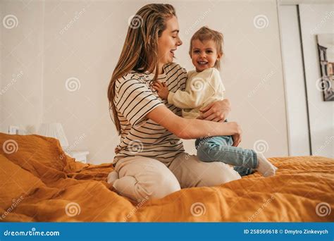 joyous female parent embracing  child seated   bedroom stock