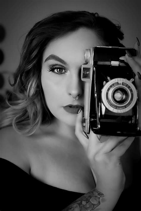 A black and white photoshoot of a woman holding a retro camera up to