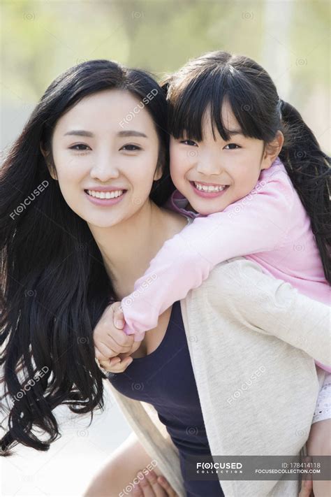 Asian mother riding daughter piggyback — outside, cheerful - Stock