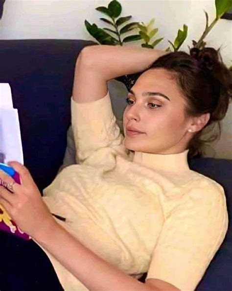 a woman sitting on a couch reading a book with her hands behind her ...