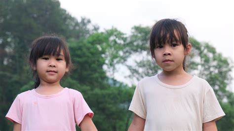 Two cute Asian sisters holding hands standing in the summer garden