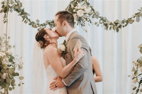 a bride and groom kissing in front of an arch of greenery at their wedding