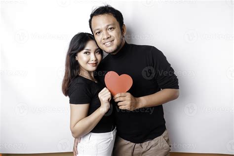 A young Asian couple smiling and holding red heart-shaped paper