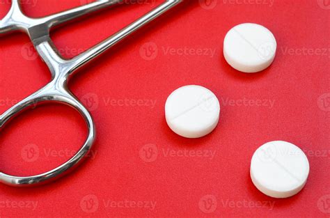 Several white tablets and a medical clamp lie on a bright red