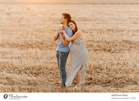 Couple awaiting baby hugging in field - a Royalty Free Stock Photo from Photocase