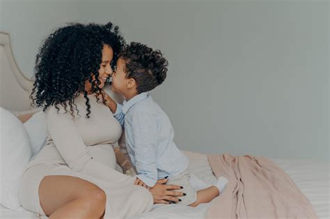 mère afro-américaine et petit fils assis sur le lit et se touchant avec