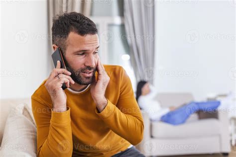 Young Man Talking Privately On Cell Phone While His Wife is watching tv