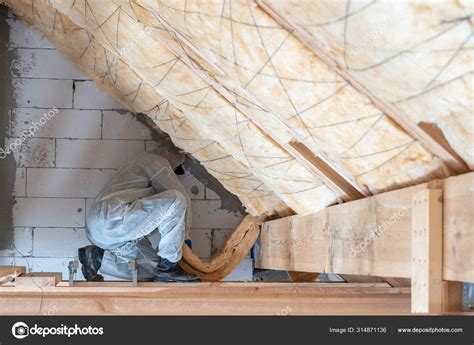 Professional workman installing thermal insulation layer under the roof ...