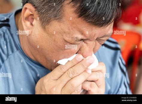 close   asian man sneezing  tissue paper covering mouth