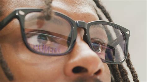 A young black man with dreadlocks and glasses looking at the computer ...