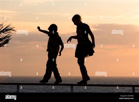 Silhouette of children walking on a railing at sunset by the sea Stock ...