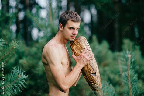 Odd primitive naked man with huge wooden stick hunting in forest. Adult