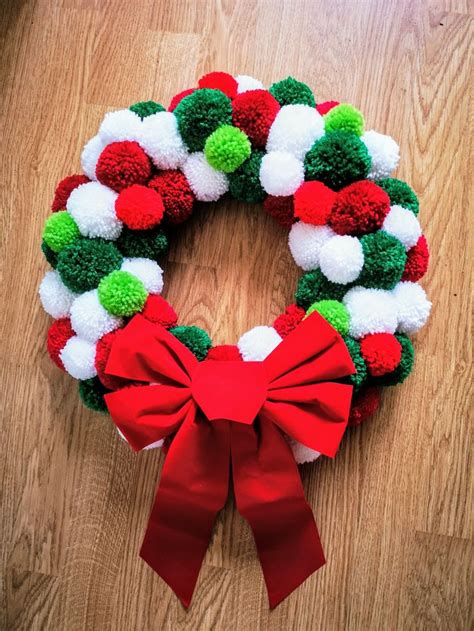 a christmas wreath with pom - poms and a red bow on the floor