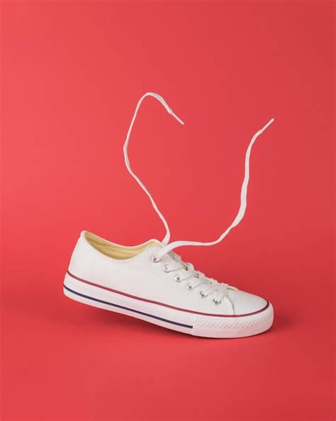 White sports sneakers with a red stripe with flying laces on a red background | Premium Photo