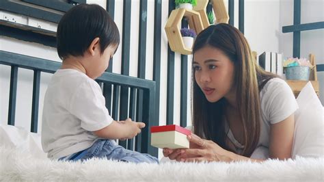 Asian mother and son play happily exchange birthday gift boxes in bed