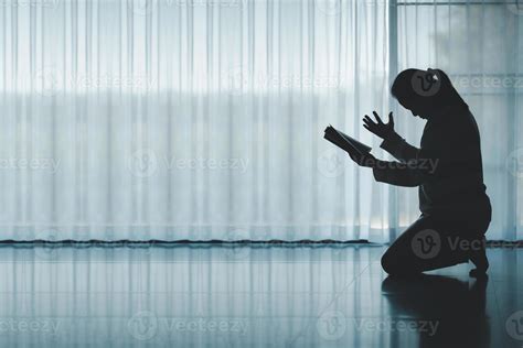 silhouette of woman kneeling and praying in modern church at sunset