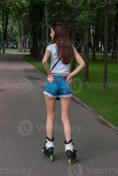 Slim brunette teen in denim shorts riding in the Park, rollerblading