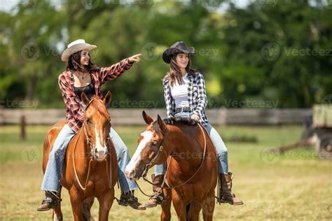Two cowgirls patroling the ranch ride their horses with one pointing on