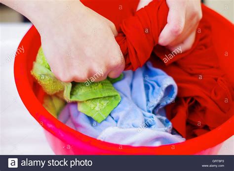 Closeup womans hands handwashing clothes in red plastic washbucket ...