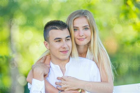 Beautiful young girl hugging her dark-haired boyfriend from behind