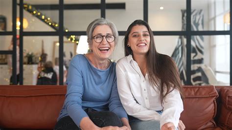 Older woman and young woman sit on a couch facing camera while talking