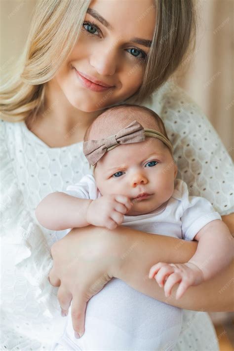 Joven madre hermosa con ojos azules sostiene a su pequeña hija recién