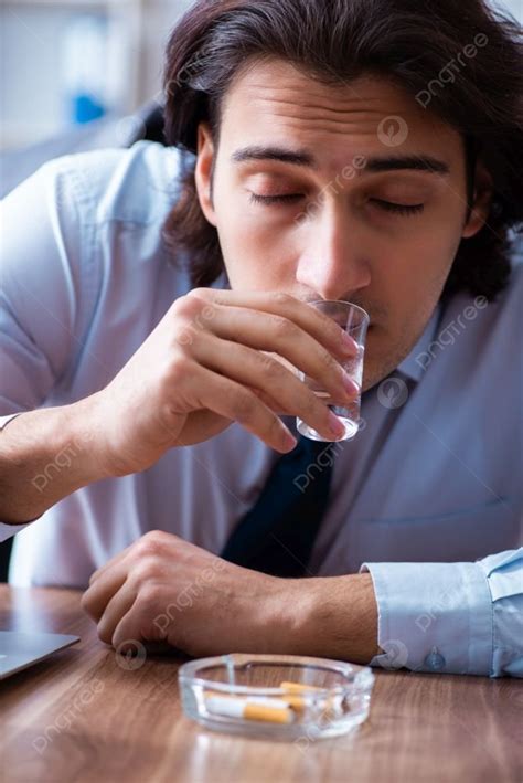 The Male Employee Drinking Vodka And Smoking Cigarettes At Workplace