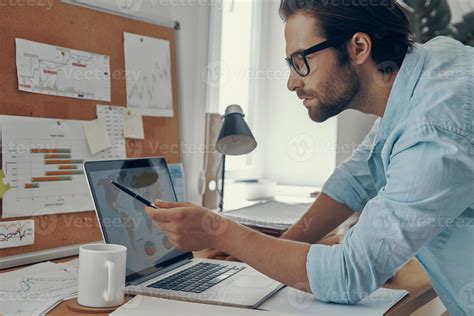 Concentrated young man analyzing data while using laptop in office