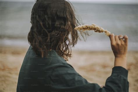 Happy young woman taking off wet white shirt on beach, back view